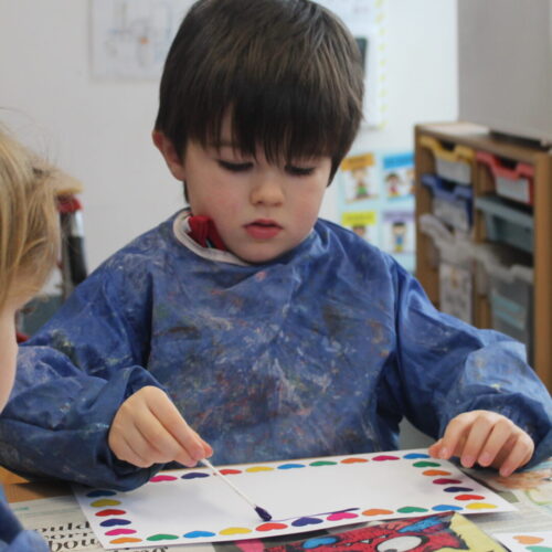 A boy from the K2 class with a painting cloak on painting a picture