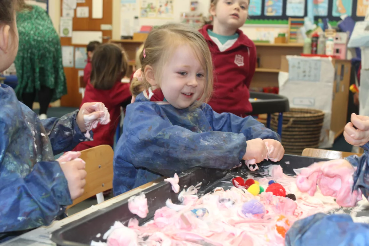 A pupil from early years with her hands in colourful foam for messy play