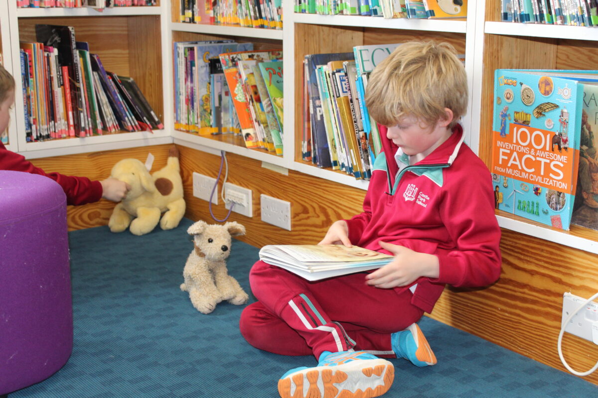 Pupil sitting comfortably on the library floor reading a book