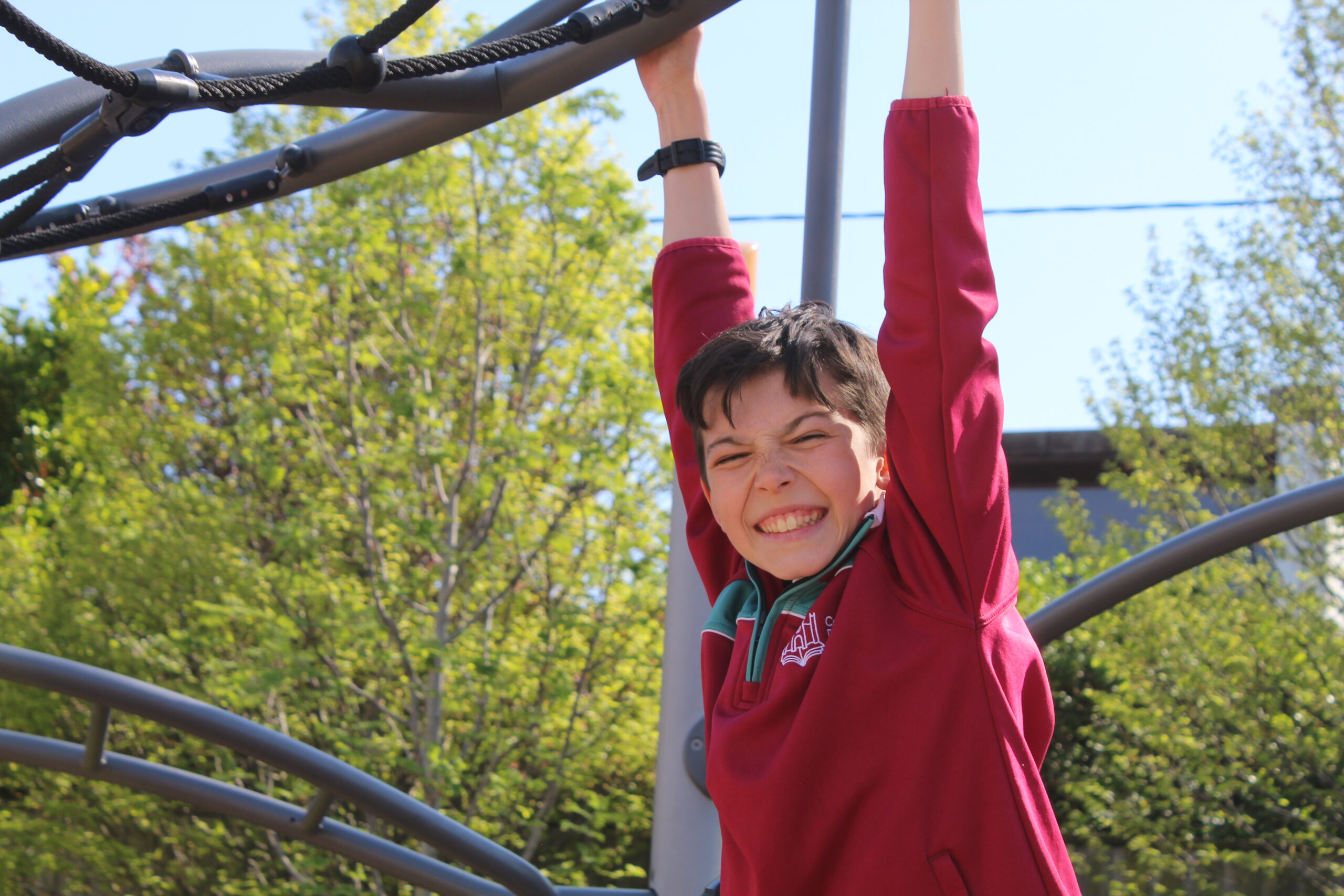 IV Pupil swinging from bars in the adventure playground with a smile